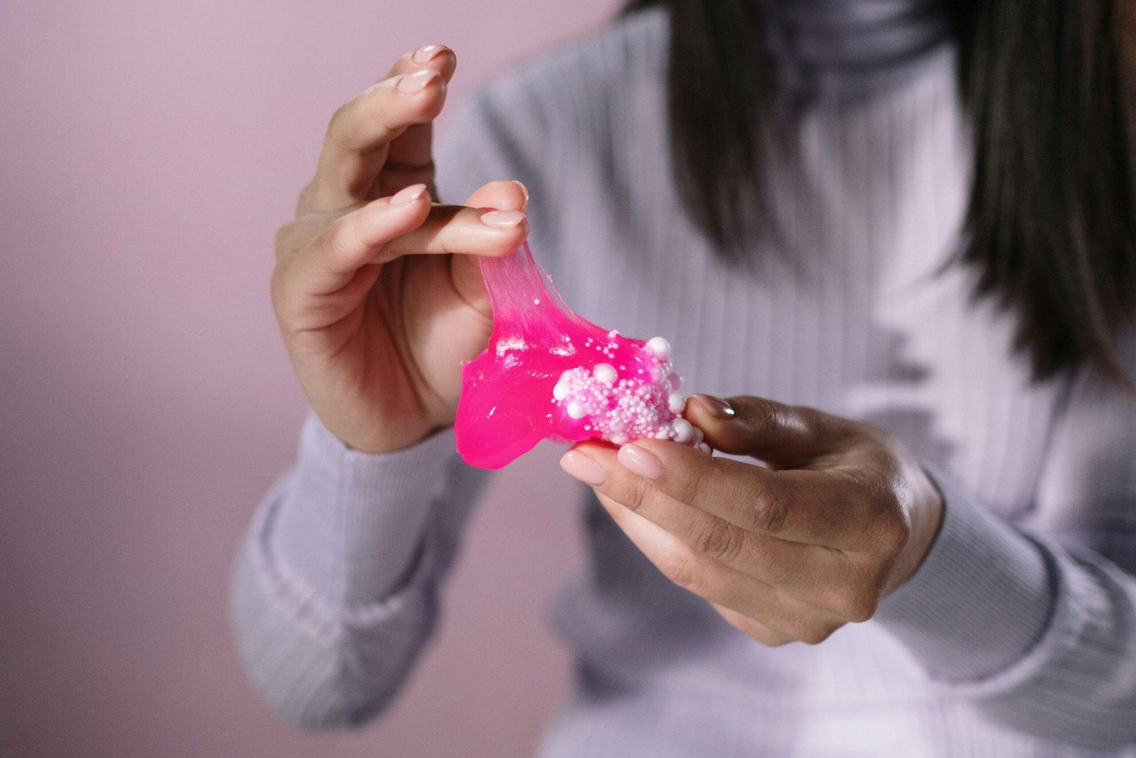 Close-up of hands stretching pink slime with foam beads, showcasing texture and tactile sensation.