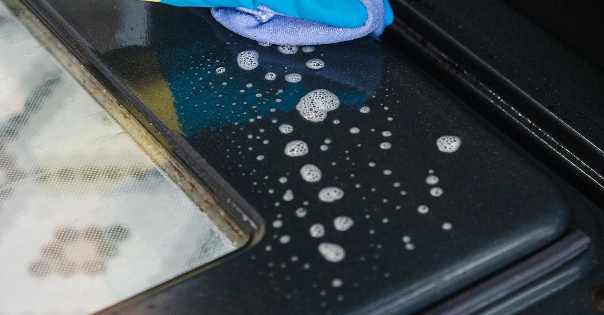 Close-up of cleaning an oven door with gloves and detergent in a kitchen.